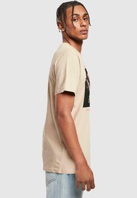 Beige bomulds T-shirt med korte ærmer, med et fremtrædende grafisk design på forsiden, løs pasform, blød tekstur og rund halsudskæring.