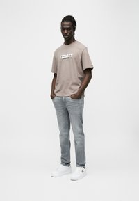 Γκρι κοντομάνικη μπλούζα με λευκή επιγραφή "TOMMY JEANS", σε συνδυασμό με τζιν ανοιχτού χρώματος και λευκά αθλητικά παπούτσια. Λείο ύφασμα, άνετη εφαρμογή.