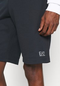 Shorts in cotone blu marina con una texture liscia, caratterizzati da un logo bianco ricamato all'orlo e una vita elastica per il comfort.