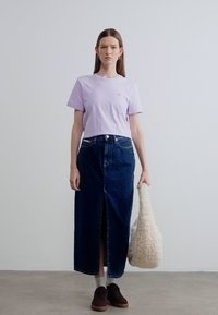 Μωβ κοντομάνικη μπλούζα σετ με μακριά φούστα από σκούρο τζιν με ψηλή μέση και σκίσιμο μπροστά. Το μοντέλο κρατά μια αφράτη μπεζ τσάντα.