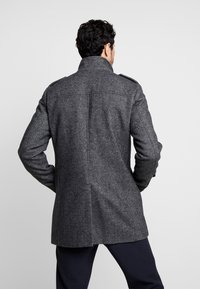 Grå ullblandad kappa med krage, strukturerade axlar och en texturerad yta. Har en ren baksidestil och en skräddarsydd passform.