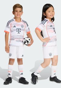 Detské futbalové súpravy Adidas obsahujú biely dres s šedými a korálovými akcentmi, čiernymi logami a zodpovedajúcimi šortkami. Súčasťou sú aj čierne kopačky a biele ponožky.