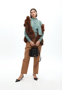 Zelený pletený top, hnědý kabát z umělé kožešiny, béžové kalhoty, černá prošívaná kabelka se zlatými doplňky a černé lodičky na jehlovém podpatku s akcenty.