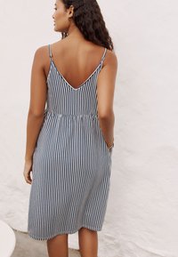 Robe midi rayée avec dos en V, fines bretelles, taille élastique, couleurs bleue et blanche, poches latérales, fabriquée en tissu léger.