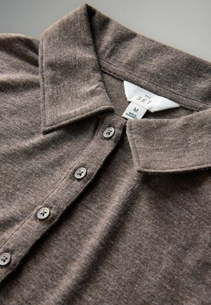 Kohvane kootud polo särk pehme tekstuuriga, kraega, viie halli nupuga ja etiketiga, mis näitab suurust M, valmistatud Bangladeshis.