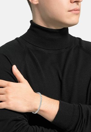 Bracciale in argento sulla polso, con anelli intercalati. L'indossatore è vestito con un maglione nero a collo alto con una texture a coste.