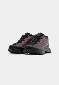 Black trail running shoes with pink accents, a textured upper, rugged outsoles, and a secure lace system for stability and grip.