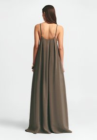 Maxiklänning i olivgrön, tillverkad av l�ättviktig tyg. Har tunna band, en flödande silhuett och en slät yta. Rygglös design.