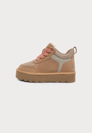 Zapatilla deportiva de plataforma en ante marrón con cordones rojos y blancos, detalle gris en el lateral, suela gruesa y forro interior blanco sobre un fondo liso.
