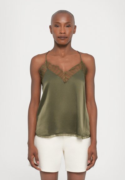 Olivgrünes Satin-Camisole mit durchsichtigen, texturierten Akzenten am Ausschnitt und verstellbaren Trägern, kombiniert mit cremefarbene Shorts.