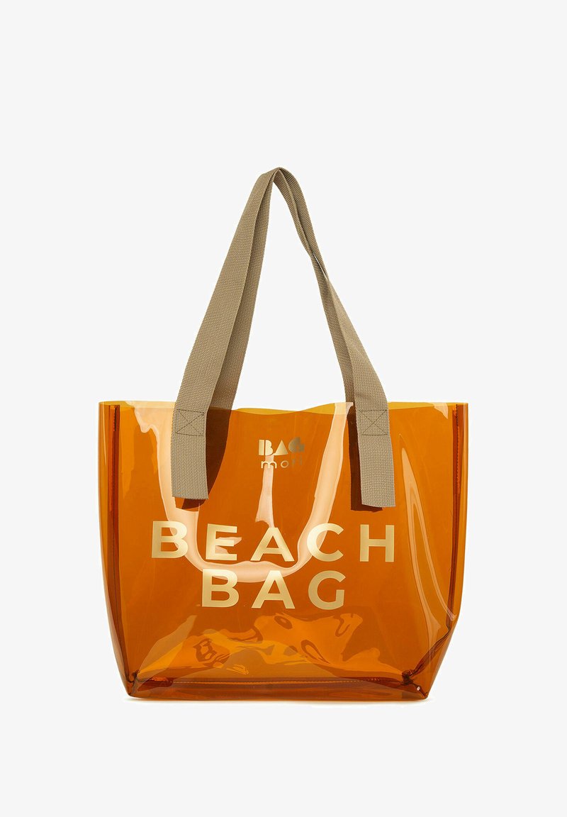 Oranssi läpinäkyvä rannakassi vaaleanbeigeistä kankaasta valmistetuilla kahvoilla. Kassi on varustettu kultaisella tekstillä "BEACH BAG" ja siinä on tyylikäs, moderni muotoilu.