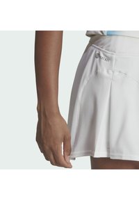 Plissé witte tennisrok van textuurstof, met een subtiele logo en een elastische tailleband. De zoomlijn is recht en netjes.