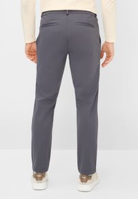 Grijze broek van glad materiaal, met een strakke pasvorm, achterzakken en een elastische tailleband, gecombineerd met lichtgekleurde sneakers.