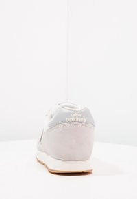 Baskets en daim gris clair avec une tige en cuir blanc et une semelle en caoutchouc beige. Dotées du logo "New Balance" sur le talon en gris avec des accents beiges.