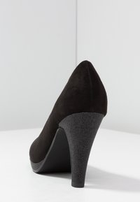 Chaussure à talons aiguilles en suède noir avec un bout pointu et un talon texturé gris foncé. Le talon présente un effet scintillant subtil.