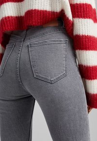 Šedé skinny džíny s dvěma zadními kapsami, elastická tkanina a jemně strukturovaný povrch. V kombinaci s pleteným svetrem s červenými a bílými pruhy.