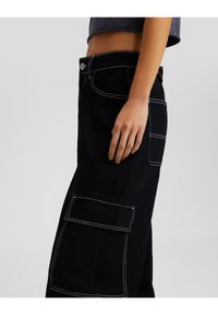 Pantalones cargo negros con costuras blancas en contraste, que presentan grandes bolsillos laterales y una cintura ajustada, fabricados con un tejido duradero.