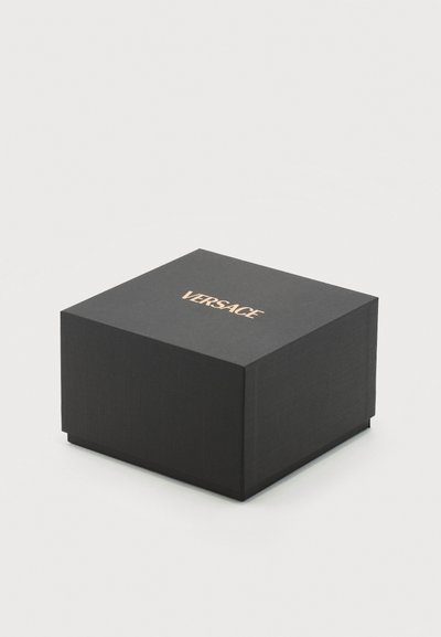 Juodas kvadratinis dėžutė su auksiniu "Versace" logotipu centre viršuje, pastatyta ant paprasto šviesiai pilkos spalvos fono.
