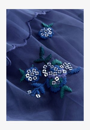 Tamsiai mėlynas permatomas audinys su siuvinėtu gėlių raštu mėlynos ir žalios spalvos, pabrėžtas apskritais sidabriniais blizgučiais ir banguotu kraštu.