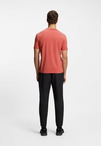 Coral short-sleeve t-shirt paired with black joggers. T-shirt has a round neckline; joggers feature elastic cuffs and a smooth texture.