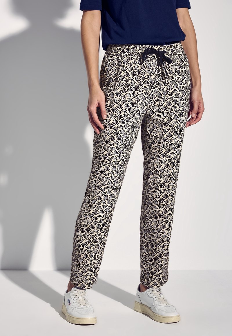 Pantalon à motifs avec un dessin floral noir sur fond beige. Ils disposent d'une ceinture élastique avec un cordon de serrage et des jambes droites.