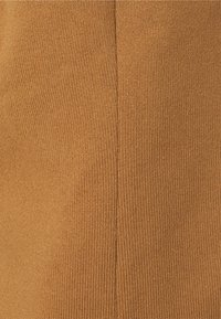 Prążkowana, teksturowana tkanina w ciepłym brązowym kolorze z pionowym szwem. Materiał jest elastyczny i lekko błyszczący.