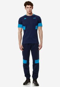 Top deportivo azul marino con acentos turquesa, mangas cortas y pantalones ajustados a juego que cuentan con bolsillos laterales y bloques de color contrastantes.