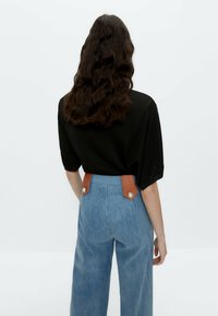 Sort ribbet top kombineret med højttaljede lyseblå denimbukser med brune læderdetaljer og fremtrædende knapdetaljer.