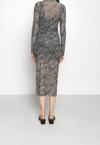 Pitkähihainen, läpikuultava, mustavalkoinen kuvioitu mekko, joka on kapea ja ulottuu hieman polven alapuolelle, ja siinä on hieman vyötärön yhtenäisyys.