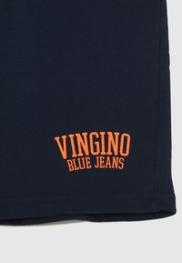 T-paita tummansinisellä värillä, jossa on oranssilla brodeerattu teksti "VINGINO BLUE JEANS". Pehmeä kangas, normaali istuvuus ja lyhyet hihat.