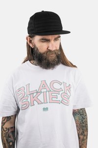 Fekete sapka varrásmintával és lapos szélekkel, fehér pólóval, amelyen "BLACK SKIES" felirat olvasható pink és türkiz színben.