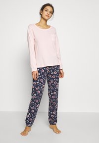 Zachtroze lange mouwen top met een zak, gecombineerd met marineblauwe broeken met bloemenprint en elastische manchetten. Gemaakt van zacht katoen, met een relaxte pasvorm.