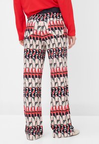 Wide-leg trousers featuring a vibrant geometric pattern in red, black, and cream; made of lightweight fabric with a smooth texture.
