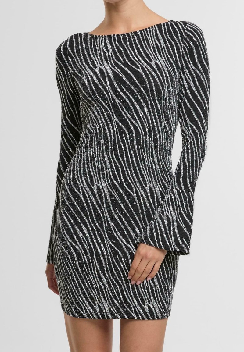 Mini-robe noire manches longues avec motif rayé ondulé argenté, silhouette ajustée, portée par une personne debout avec une main posée sur la cuisse.