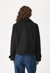 Black cropped coat with a collar, featuring long sleeves and buttoned cuffs. Paired with high-waisted blue jeans, showcasing a classic fit.