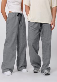 Svarta och vita randiga vida byxor med dragsko, featuring en texturerad tyg, tillsammans med en lös, ljus färgad topp och sneakers.