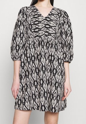 Černé a krémové šaty s výstřihem do V, nafouklými rukávy a vzorovanou strukturou obsahující prodloužené diamantové tvary. Rozšířená sukně.