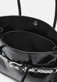 Czarna skórzana torba na ramię o błyszczącej powierzchni, z metalową klamrą w kolorze srebrnym i białymi koralikami wzdłuż paska wewnątrz pojemnej komory głównej.