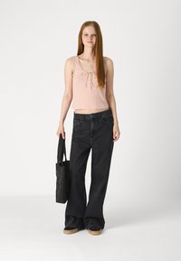 Svijetlo ružičasti rebrasti crop top s podesivim vezanjem, uparen s visokim crnim širokim trapericama. Crna prešvicana torba i platforme upotpunjuju izgled.