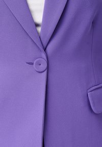 Paarse blazer met een enkele knoop, soepel materiaal en een zakdetail aan de rechterzijde. De textuur is glad en op maat gemaakt.