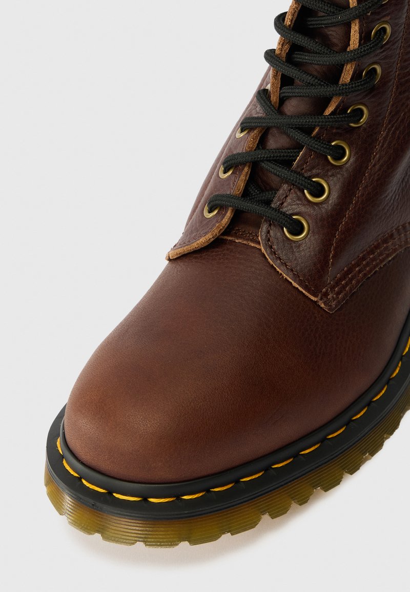 Brauner Lederstiefel mit runder Spitze, schwarzen Schnürsenkeln, gelben Nähten und einer durchsichtigen gelben Sohle mit geriffeltem Muster.