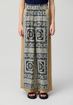 Pantaloni a gamba larga con un motivo crema e blu notte, caratterizzati da un'alta vita elastica e pannelli laterali color senape. Sandali neri.