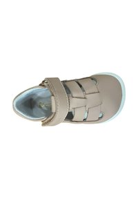 Sandalia de cuero beige con diseño de tres correas, cierre de velcro, punta redonda y suela de color azul claro. Forro interior suave visible.