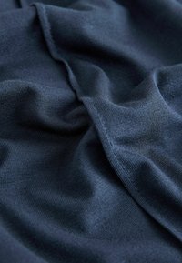 Dunkelblauer Stoff mit einer glatten Textur, der weiche Falten und dezente Stiche zeigt und eine leichte und elastische Qualität aufweist.