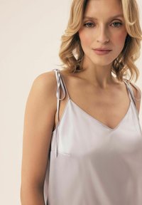 Jedwabny, jasnofioletowy top na ramiączkach z dekoltem w serek, delikatnie marszczonymi ramiączkami i gładką teksturą. Prosty i elegancki design.