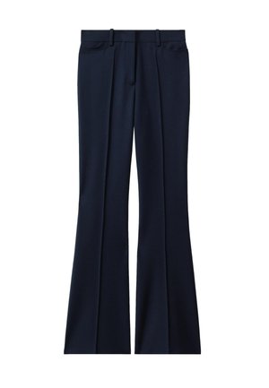 Primo piano di una persona che indossa pantaloni e giacca su misura blu scuro, regolando con una mano la giacca vicino alla vita.