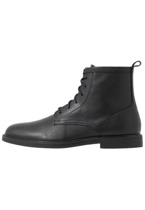 Bota de cuero negro hasta el tobillo con cierre de cordones en la parte delantera, superficie texturizada, punta redonda, tacón bajo y tira para tirar en la parte trasera.