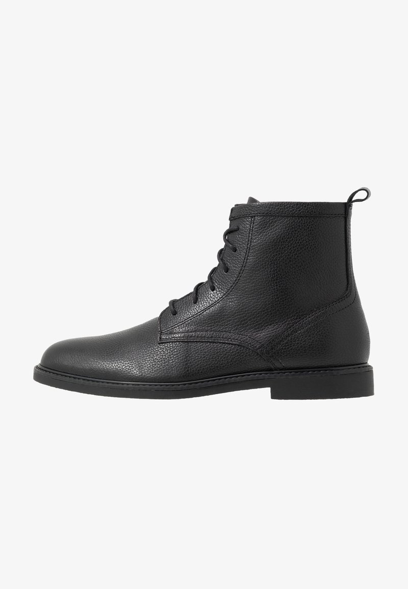 Bottine en cuir noir avec laçage à l'avant, surface texturée, bout arrondi, petit talon et languette de tirage à l'arrière.