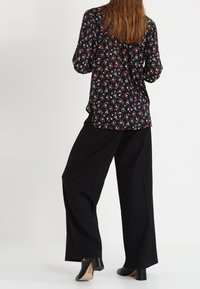 Blusa floreale con maniche lunghe nera, decorata con fiori rossi e bianchi. Abbinata a pantaloni neri larghi e scarpe con tacco a blocco.
