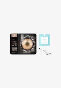 Foreo UFO 2 uppvärmd LED-maskenhetsapparat i guld och svart, tillsammans med en blå maskbehandlingsförpackning, USB-kabel och silverstöd.